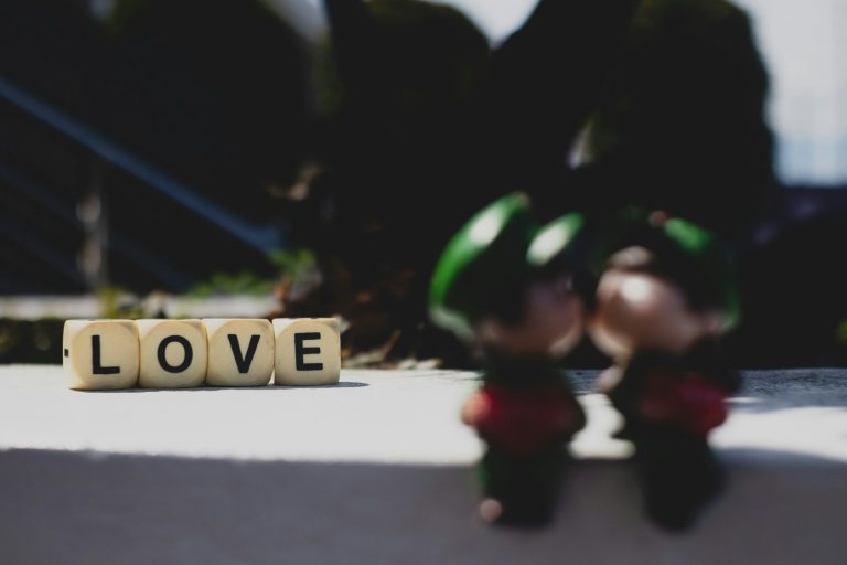 The word love is spelt out by Scrabble letters with two fuzzy toy gnomes sitting in front.